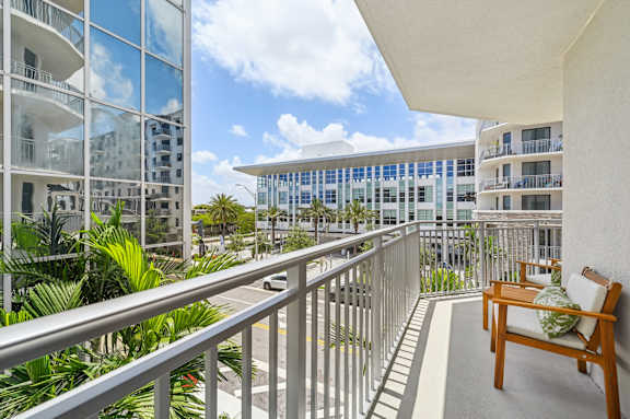 A balcony with a wooden chair and a table with a green cushion.