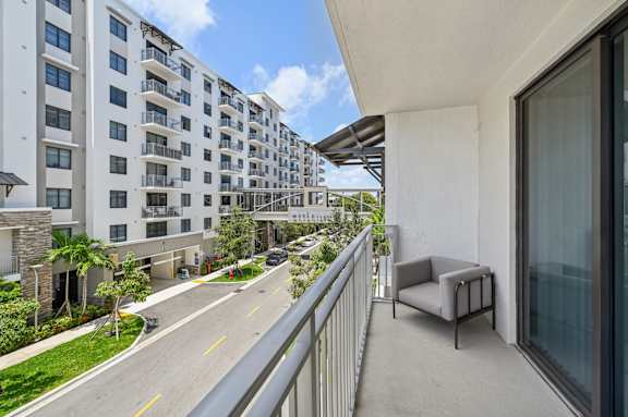 A balcony with a chair overlooks a street with apartment buildings.