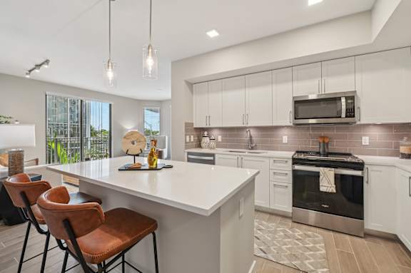 A modern kitchen with white countertops and brown leather chairs.