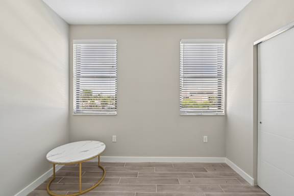 A room with a round table and two windows with blinds.