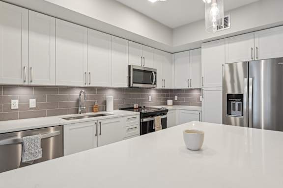 A modern kitchen with a white countertop and stainless steel appliances.