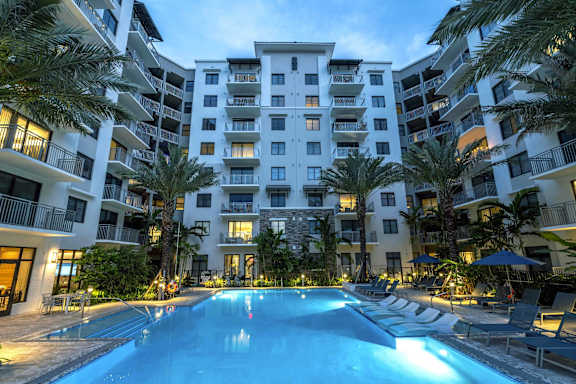 A swimming pool in front of a white apartment building surrounded by palm trees at Mayla Pompano, FL, 33062