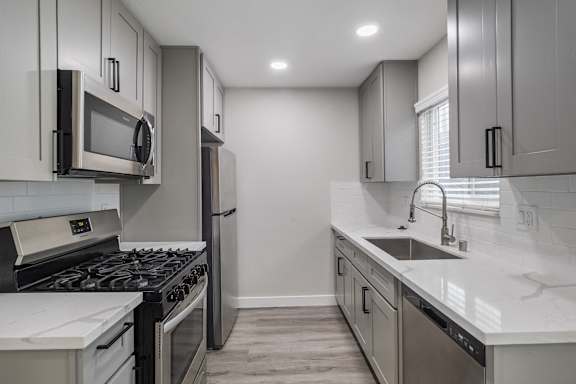 an empty kitchen with stainless steel appliances and white quartz counters