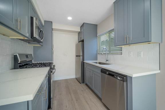 a kitchen with blue cabinets and white counter tops and a stainless steel refrigerator at Hamilton Courtyard Apartments, California