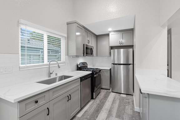 a white kitchen with stainless steel appliances and white counter tops at Hamilton Courtyard Apartments, California, 92627