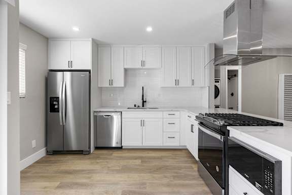 A modern kitchen with white cabinets and stainless steel appliances at Ocean Breeze Terrace Apartment, Huntington Beach
