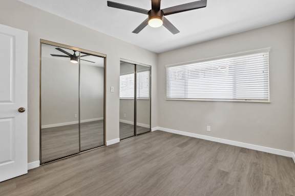 an empty bedroom with a ceiling fan and mirrored closet doors