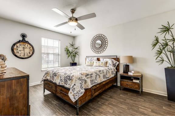 A bedroom with a bed, nightstand, and a plant.