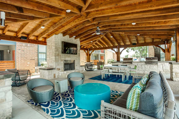A large outdoor room with a stone fireplace and a blue and white rug.