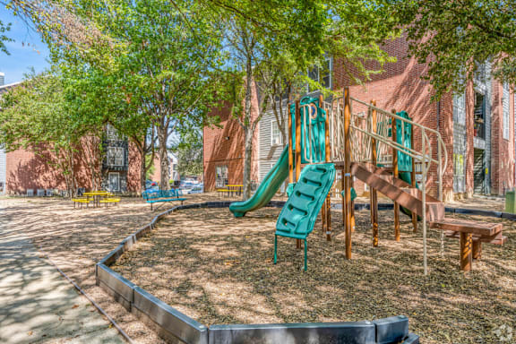 A playground with a green slide and a wooden bench.