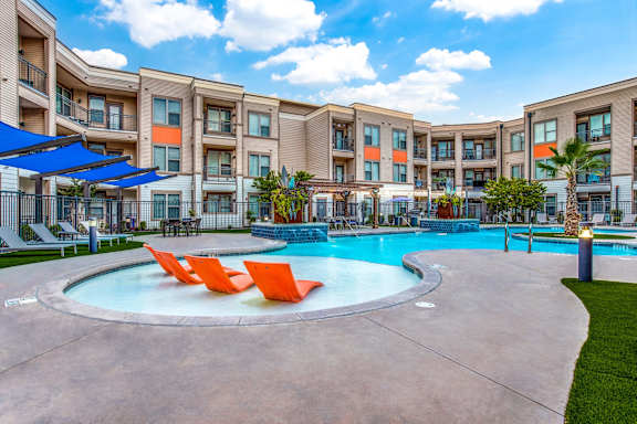 A swimming pool surrounded by orange chairs and apartment buildings.