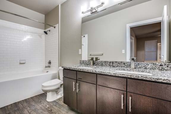 A white toilet sits in a bathroom with a marble counter top and wooden floors.