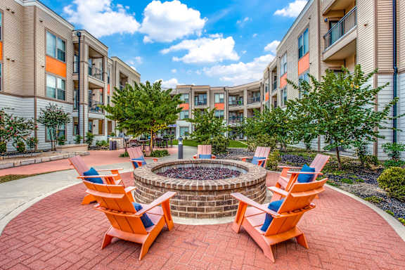 A patio with orange chairs and a fire pit in front of apartment buildings.