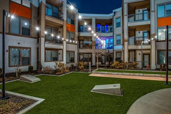 Apartment complex with a grassy courtyard and lights on the balconies.