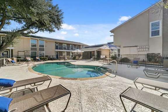 A pool surrounded by chairs and umbrellas in front of apartment buildings.