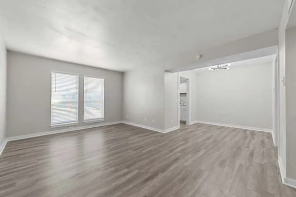 A spacious room with wooden flooring and two windows.
