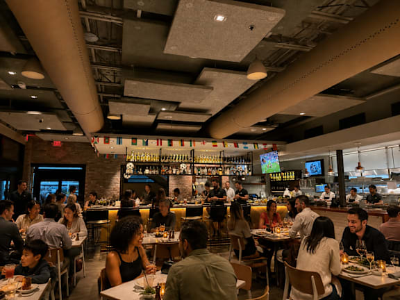 A restaurant with people dining and a bar in the background.