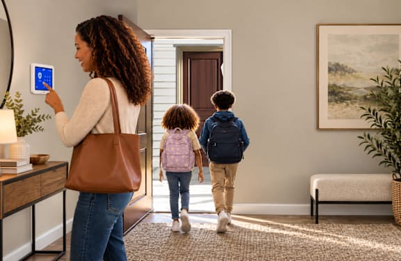 A woman is using a tablet while two children walk into the room.
