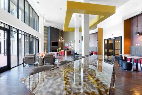 A long marble table with a yellow and white patterned runner is in the middle of a room with chairs on either side.