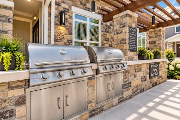 A stainless steel outdoor grill is on a stone wall.