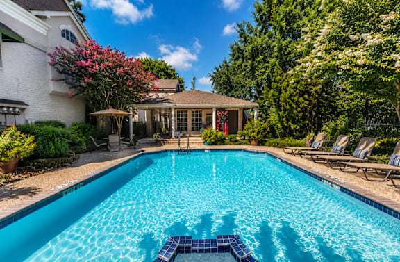 A swimming pool in a backyard with a house and trees in the background.