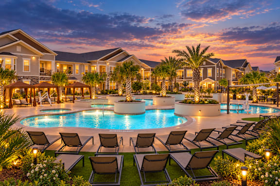 A large, luxurious pool surrounded by lounge chairs and palm trees.