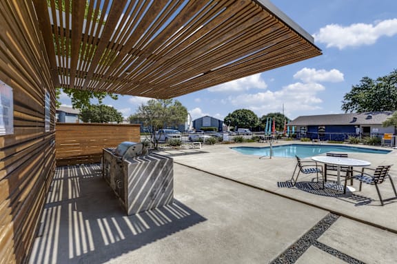 A pool area with a table and chairs under a wooden structure.