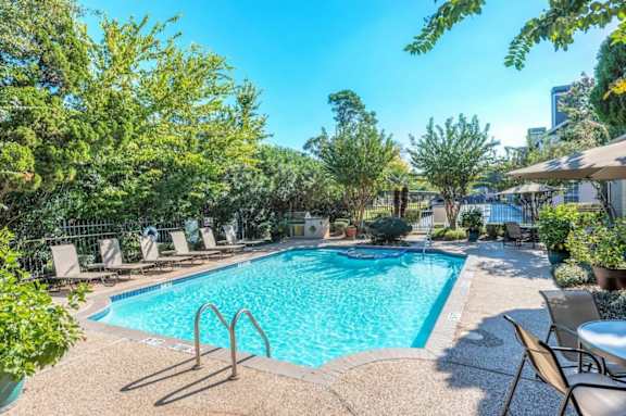 A pool surrounded by trees and chairs.