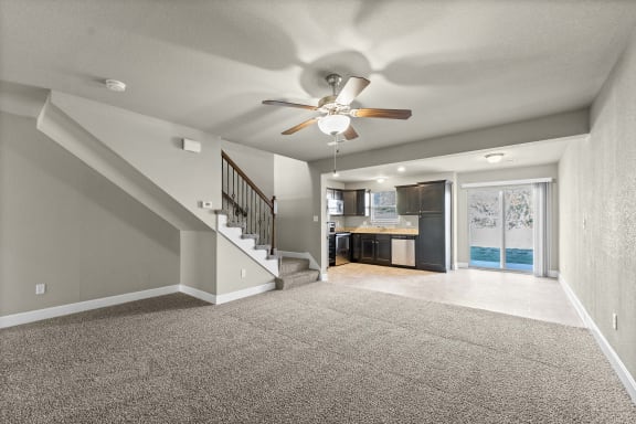an empty living room with a ceiling fan and a kitchen