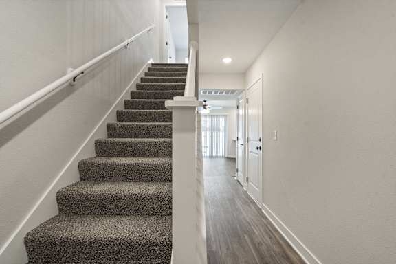 A staircase with a carpeted runner and white handrails.