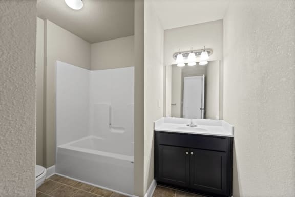 A bathroom with a white tub and sink and a black cabinet.