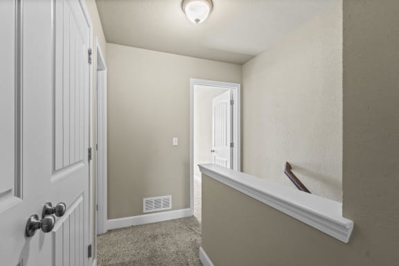 the landing of a home with a white door and a hallway with a stairwell