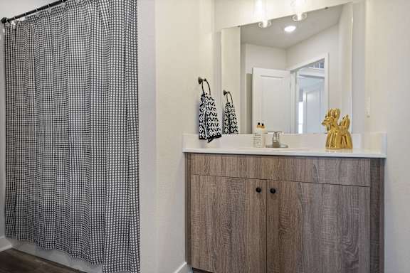 A bathroom with a shower curtain, sink, and mirror.