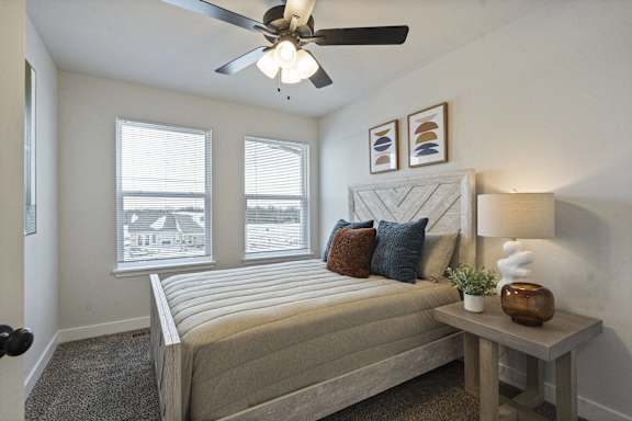 A bedroom with a bed, a ceiling fan, and a small table with a plant and a vase on it.