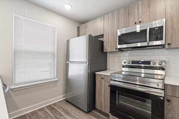 A kitchen with a stainless steel refrigerator, microwave, oven, and wooden cabinets.