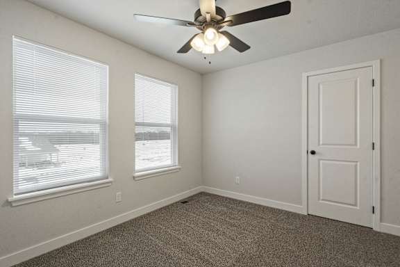 A room with a ceiling fan and two windows.