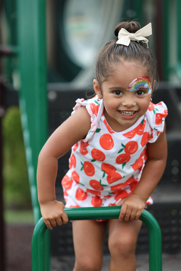 a little girl in a red and white dress playing on a green swing