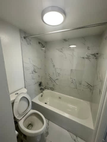A white toilet is next to a bathtub in a marble bathroom.