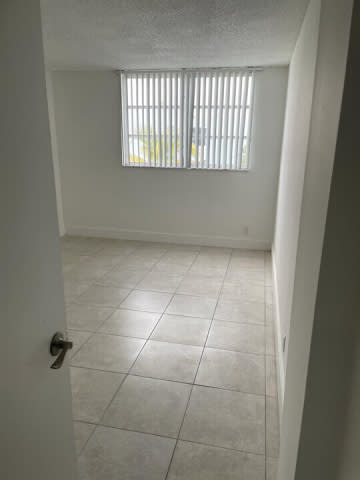 A white tiled room with a door and a window with blinds.