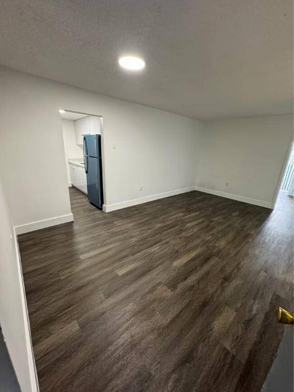 A room with a wooden floor and a blue fridge in the corner.