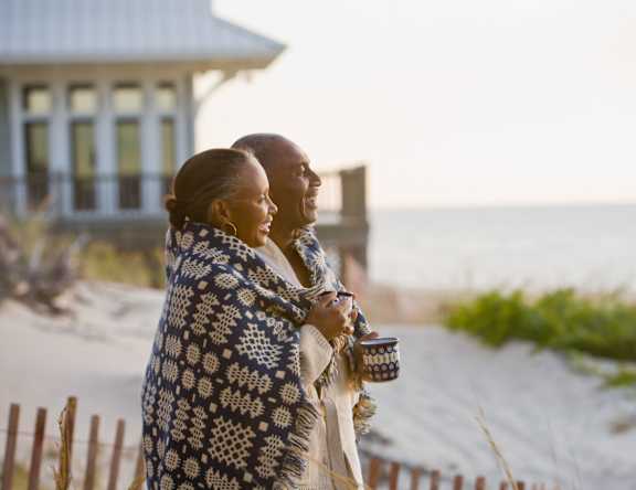 a couple wrapped in a blanket standing in front of a beach house