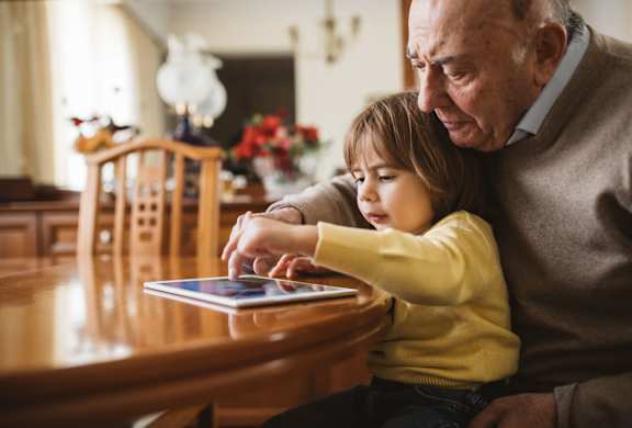an older man and a young girl are sitting at a table and looking at a tablet