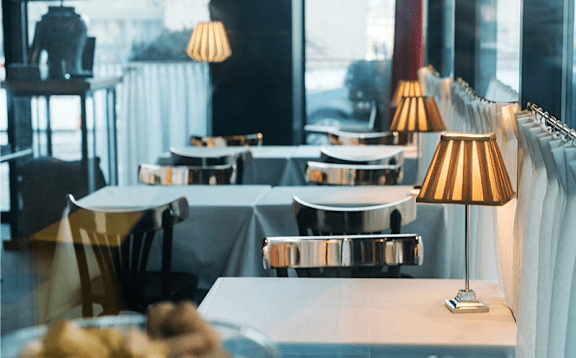 A restaurant with tables and chairs and a view of the street outside.