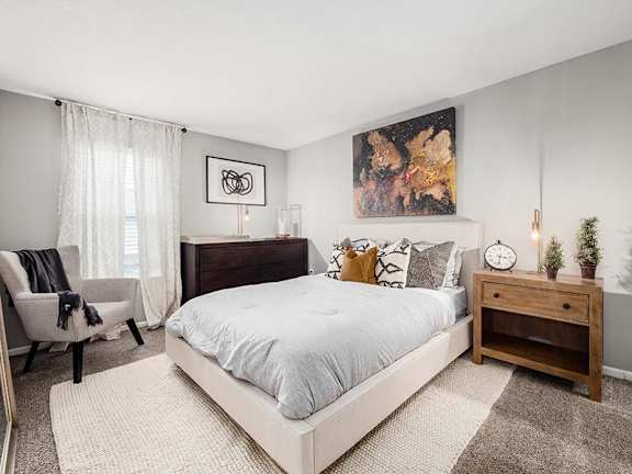 A bedroom with a large bed, a chair, and a painting on the wall.