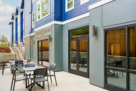 A patio with a table and chairs is outside a blue and grey building.