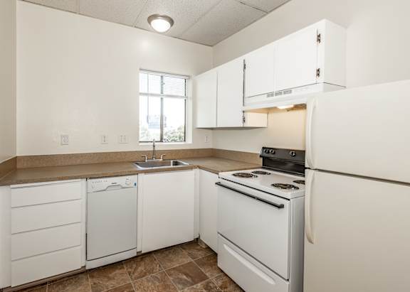 A kitchen with white appliances and brown tiles.