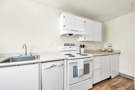 A white kitchen with a stove, sink, and cabinets.