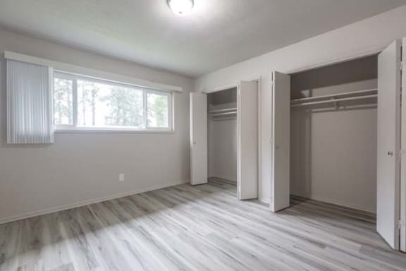 an empty bedroom with two closets and a window