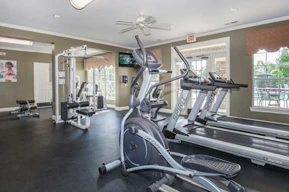 A gym with a treadmill, elliptical machines, and other exercise equipment.at Carrington Place at Wildewood Apartments, South Carolina