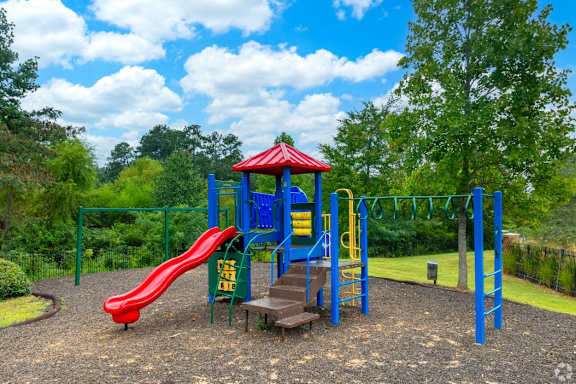 a playground with a red slide and blue playset at Magnolia Lake Apartments, Georgia 30117